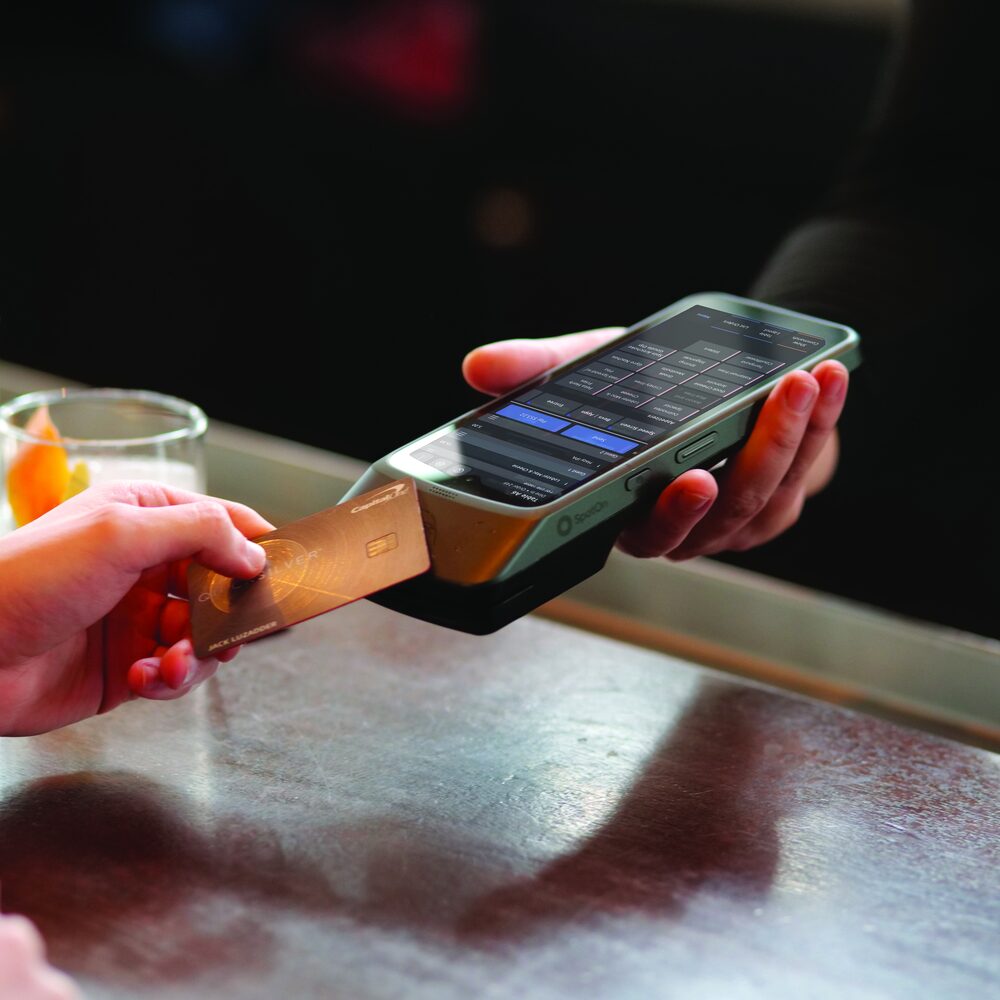 A guest tapping a card on a handheld at the bar